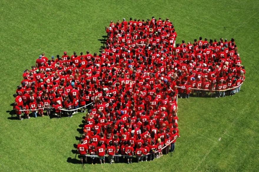 Rotes Kreuz aus Menschen auf grüner Wiese